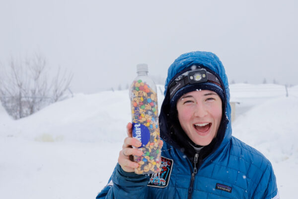 a person holds trail mix in a water bottle and smiles at the camera