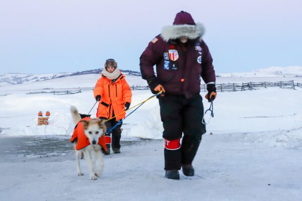 two officials walk two dogs in the snow