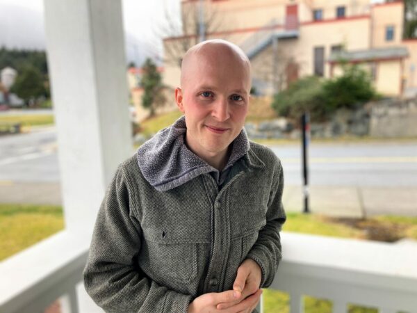 A bald young man in a Filson jacket poses for a photograph on a porch