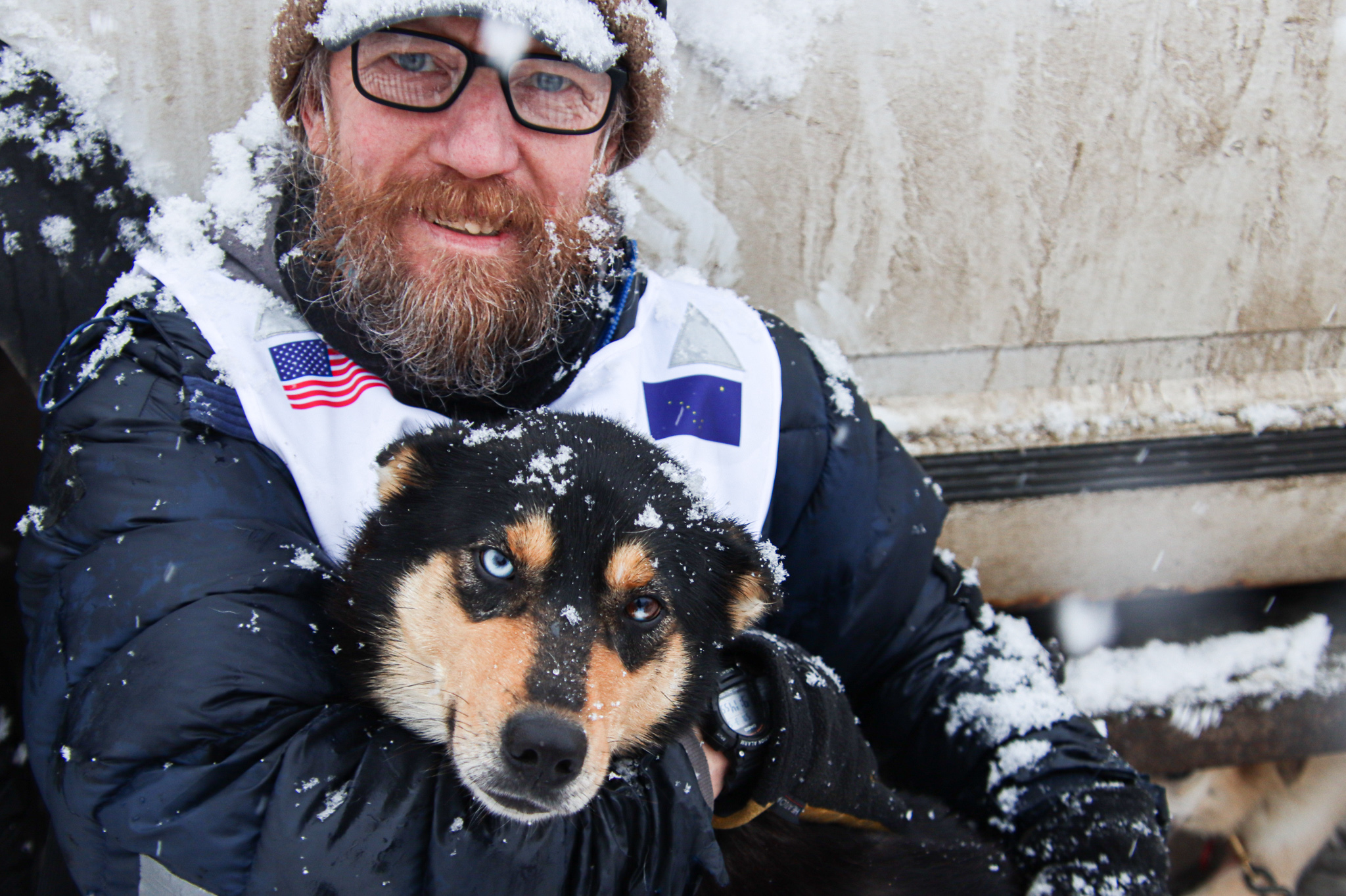 A white man with glasses and a beard holds a black and orangish dog