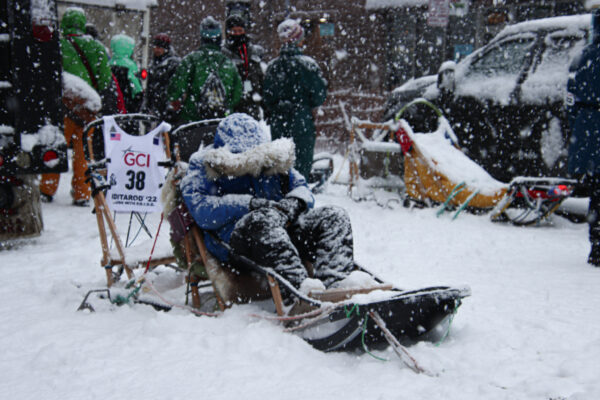 A person in a big fur-ruffed parka sleeps on a sled