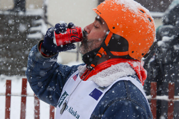 A man dressed in a denim jacket drinks a coke zero wearing an orange safety helmet