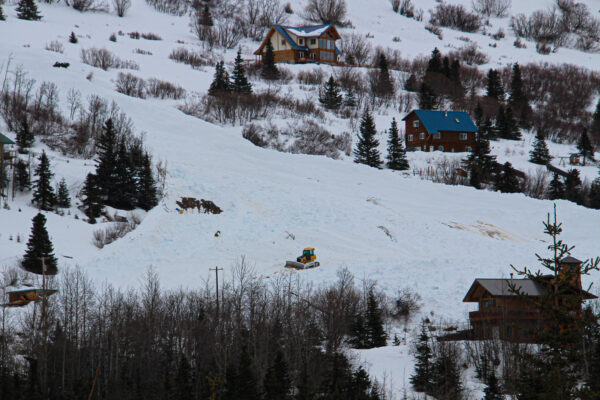 a BULLdozer on a massive avalanche next to houses