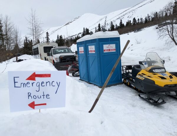 A sign that says Emergency Route next to a snow machine and outhouses