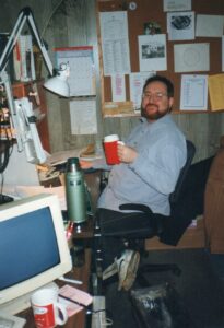 A man sitting in a newsroom holding a large plastic mug