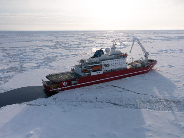 aerial view of a red research ship sailing through ice-covered water