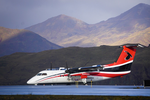 A Ravn turboprop plane on a runway with mountains behind it