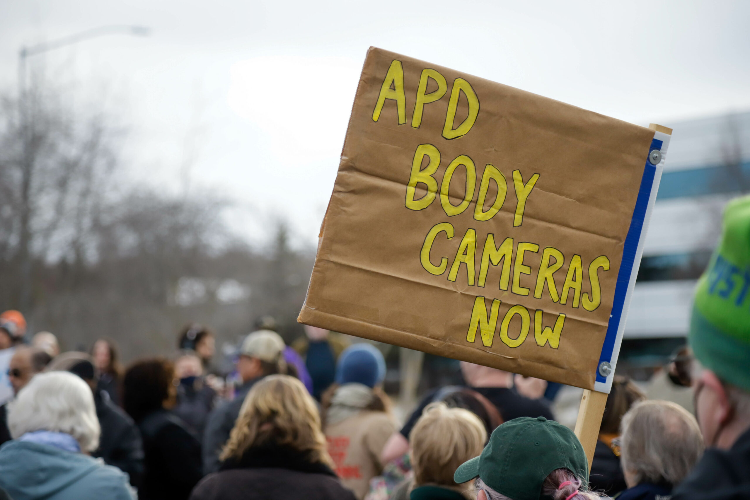 a sign at a rally that reads "APD body cameras now"