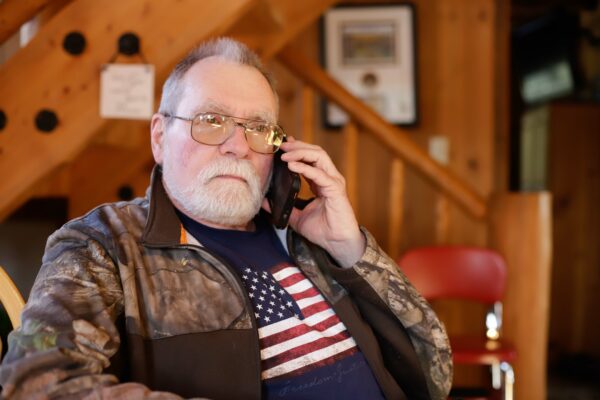 a person wearing camo and an American flag shirt holds a cell phone to his ear