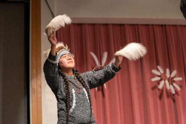 A woman waves dance fans while performing Yup'ik dance on a stage.