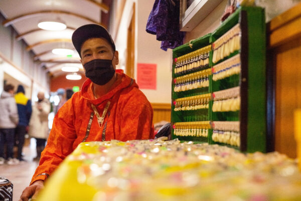 A man sits behind a table covered in ivory earrings for sale.