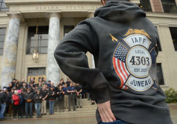 A man wearing a Local 4303 sweatshirt watches a rally on the Capitol steps in Juneau