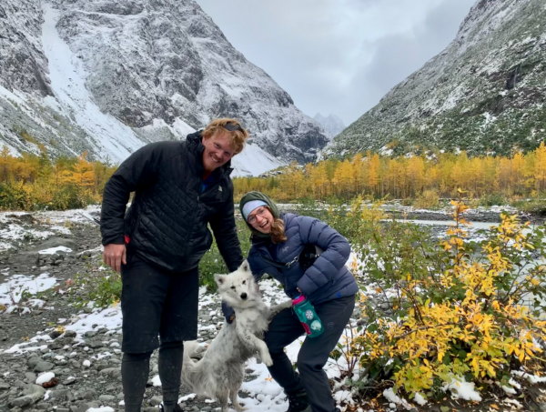 A man, woman and dog pose in front of mountains in the fall. 