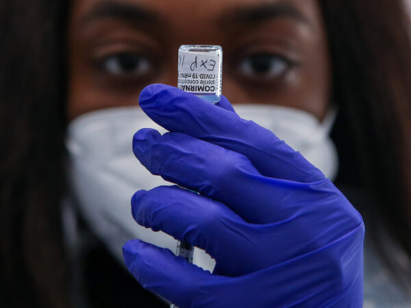 a woman in a mask pulls vaccine from a vial