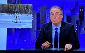 John Oliver at his desk with a photo of the Nenana tripod inset