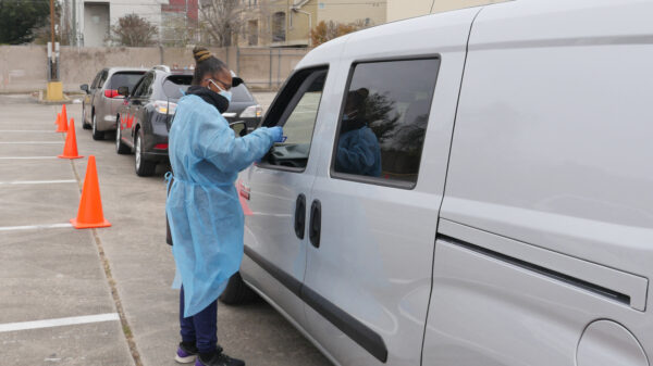 a medical worker talks to someone through their driver's side window