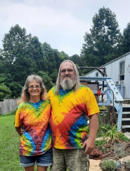 A man and woman pose outside in tie-dyed shirts