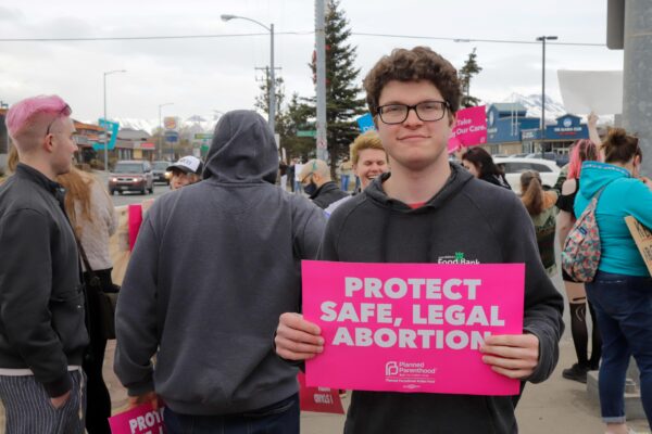 a person stands with a "protect safe, legal abortion" sign