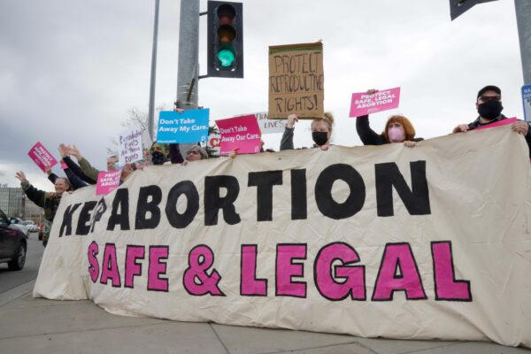 people hold up a large banner that reads "keep abortion safe & legal"