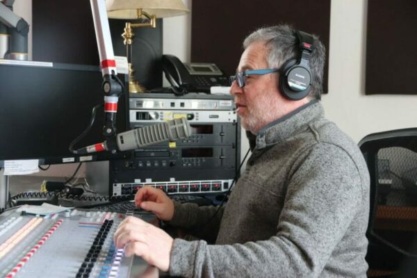 A man wearing headphones and speaking into a microphone in a radio studio