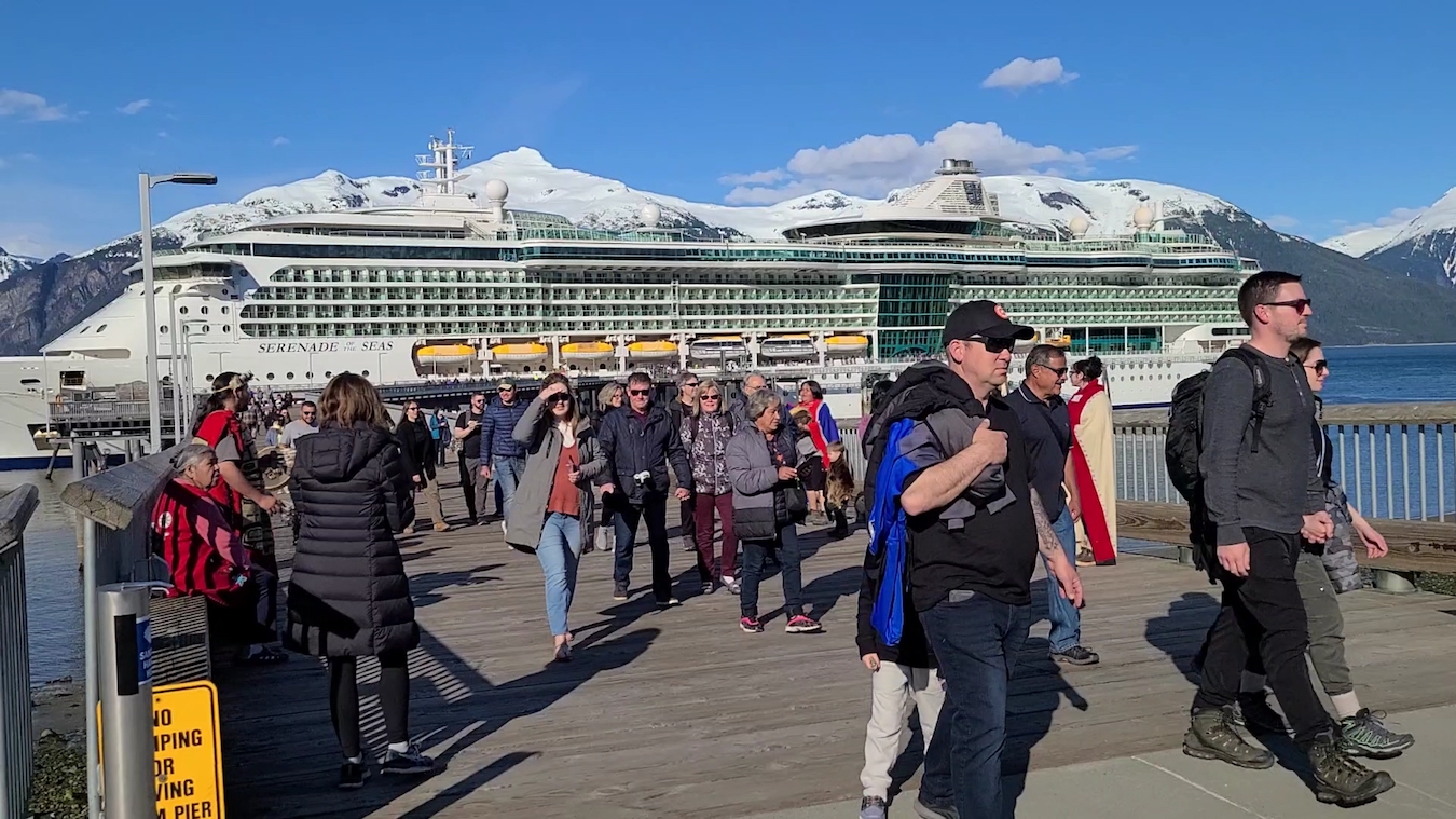 People disembark from a cruise ship on a sunny day