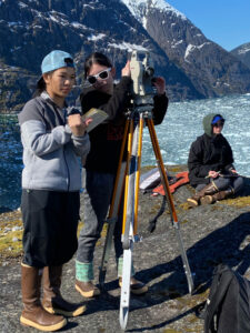 Students working with equipment on a tripod with a glacier in the background