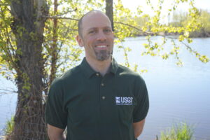 A man in a USGS golf shirt standing by some water