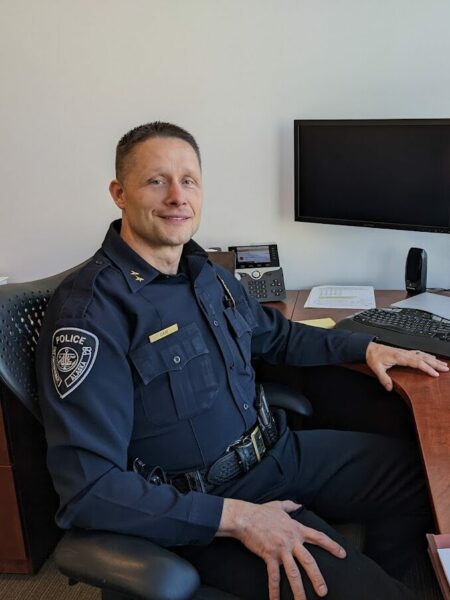 A white man in a police uniform at a wooden desk