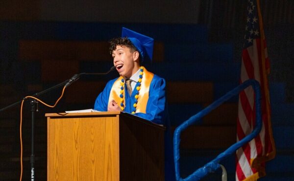 a student in a cap and gown speaks at a lectern