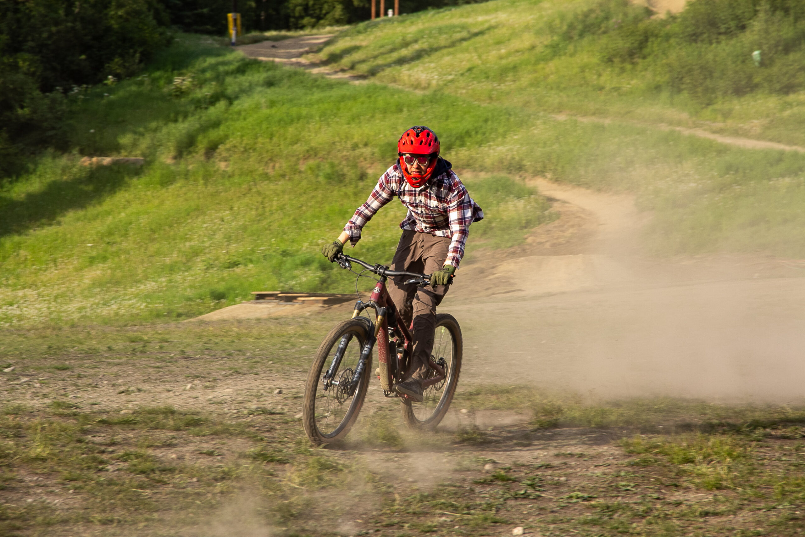 A teenage boy in a red bicycle helmet kicks up dust on a mountain bike.