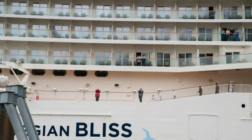 The side of a large cruise ship, with passengers visible on balconies and walkways.