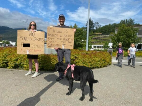 two people stand outside with signs and a dog