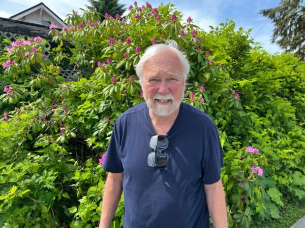 An older man standing in front of a tall hedge