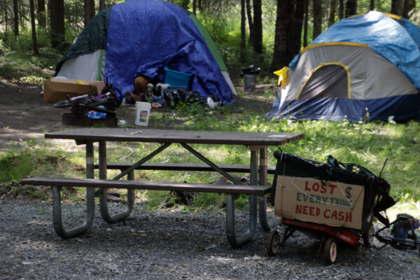 A wagon with a painted cardboard sign that says "Lost $ everything need cash" and two tents in the background