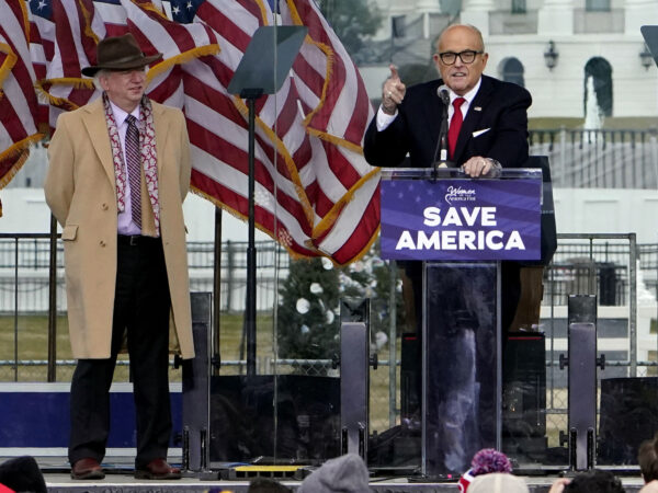 John Eastman, wearing a fedora, stands onstage next to Rudy Giuliani