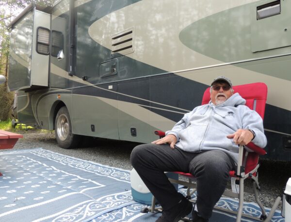 A man sits in a folding chair next to an RV