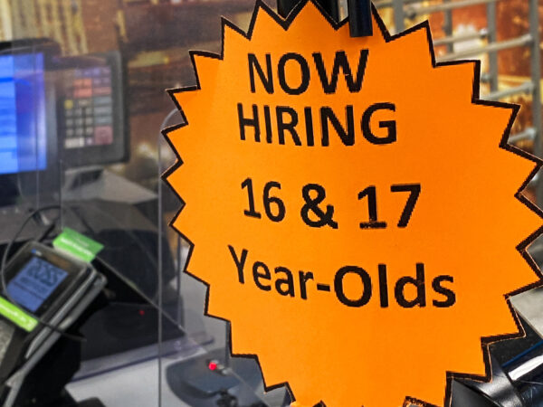 A sign in a window that says "now hiring 16 & 17 year olds"