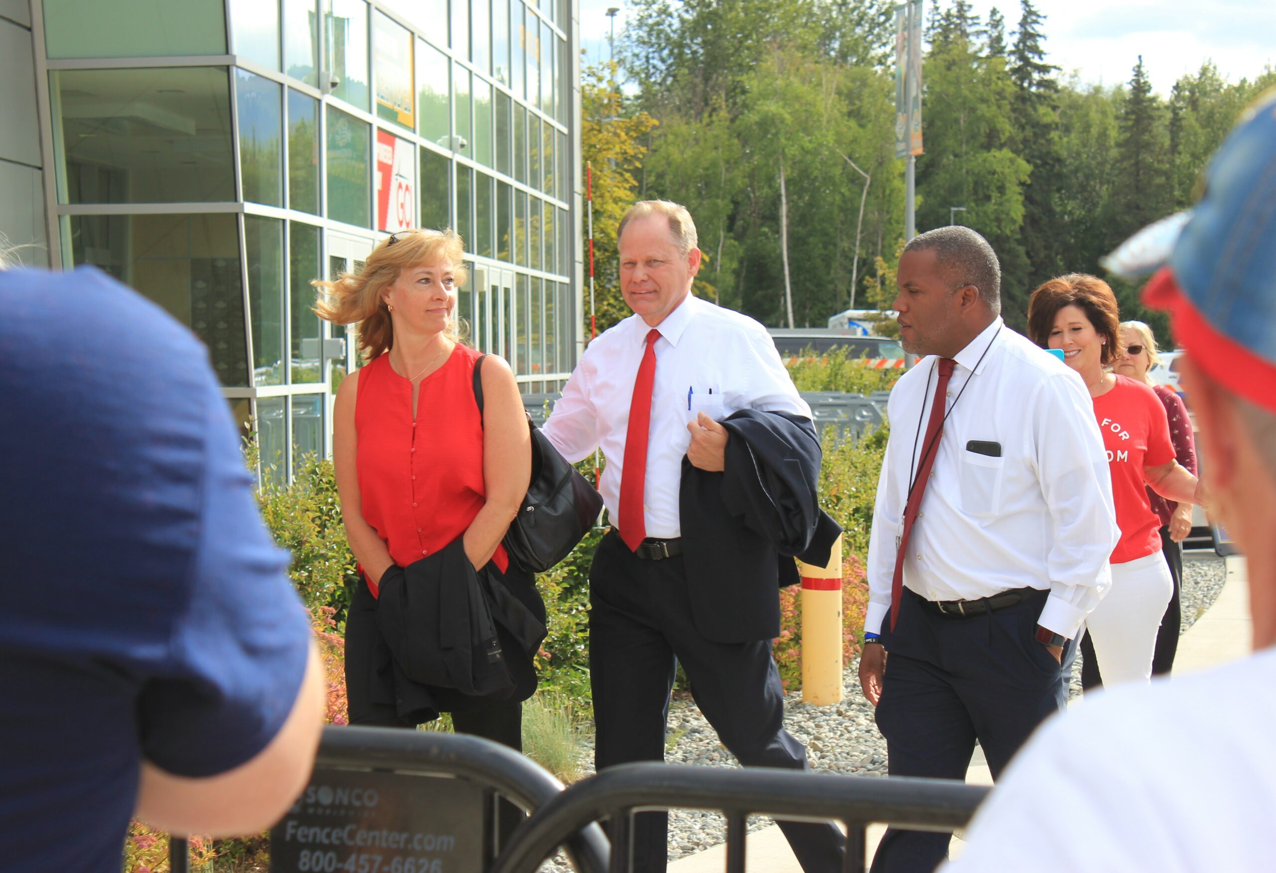 Two men in ties and a woman in a red dress walk into a building