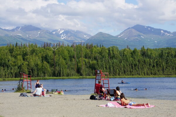 people laying on beach and swimming in water with mountains in background
