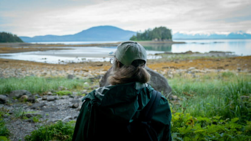 Exterior: a woman facing toward a shoreline.