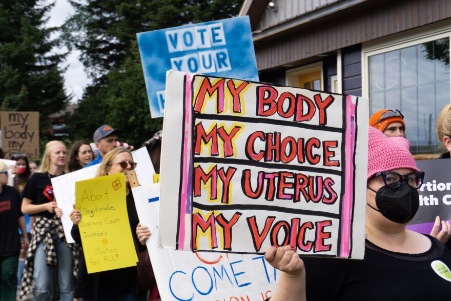 A protester holds a sign reading "My body, my choice, my uterus, my voice"