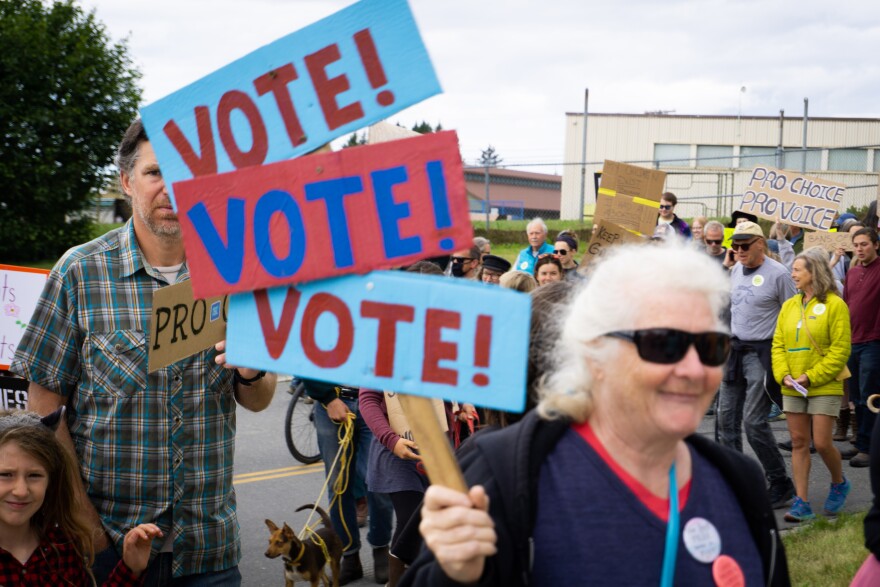 A protester holds a sign saying "Vote! Vote! Vote!"