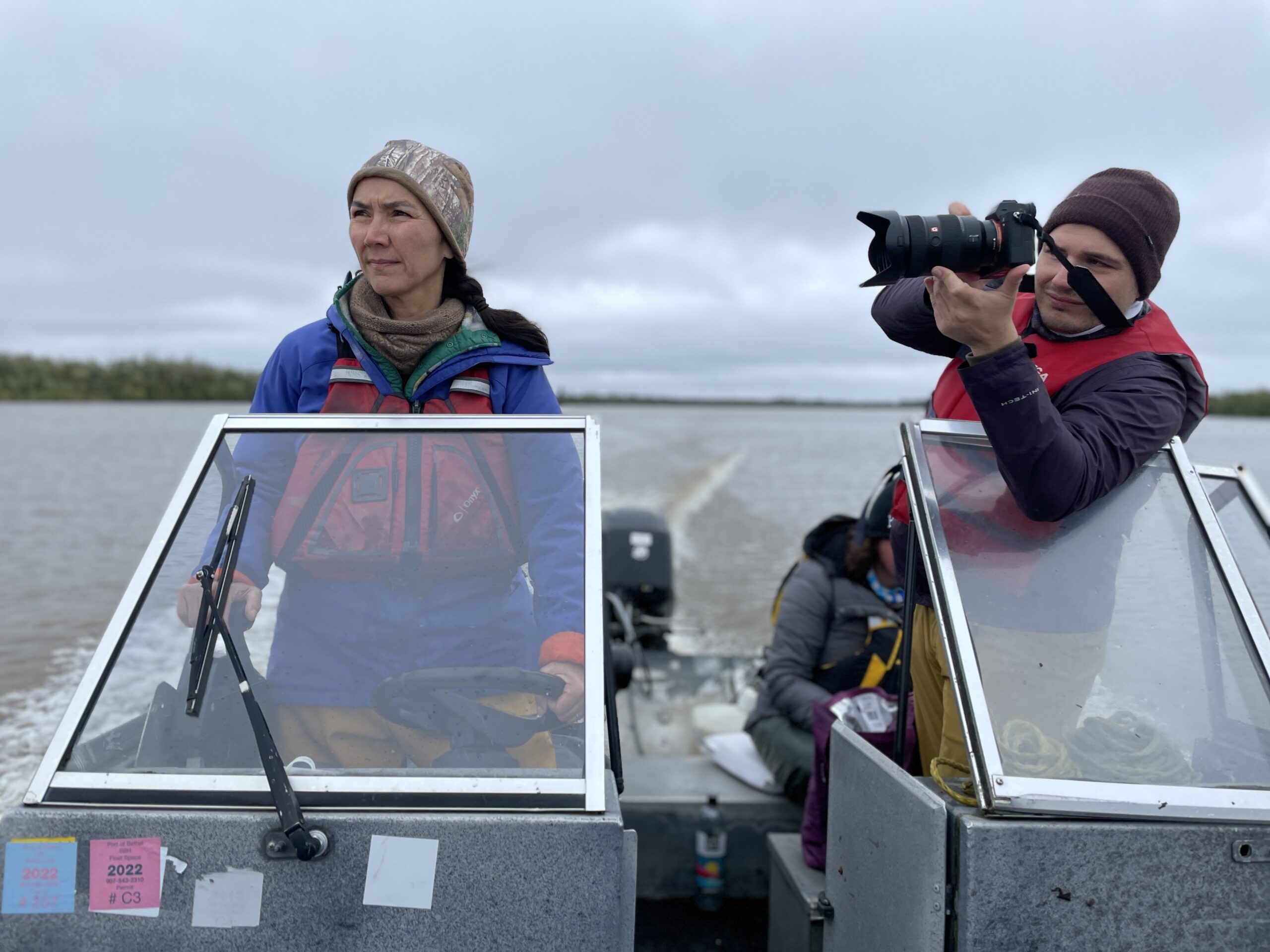 woman drives boat while passenger uses his camera