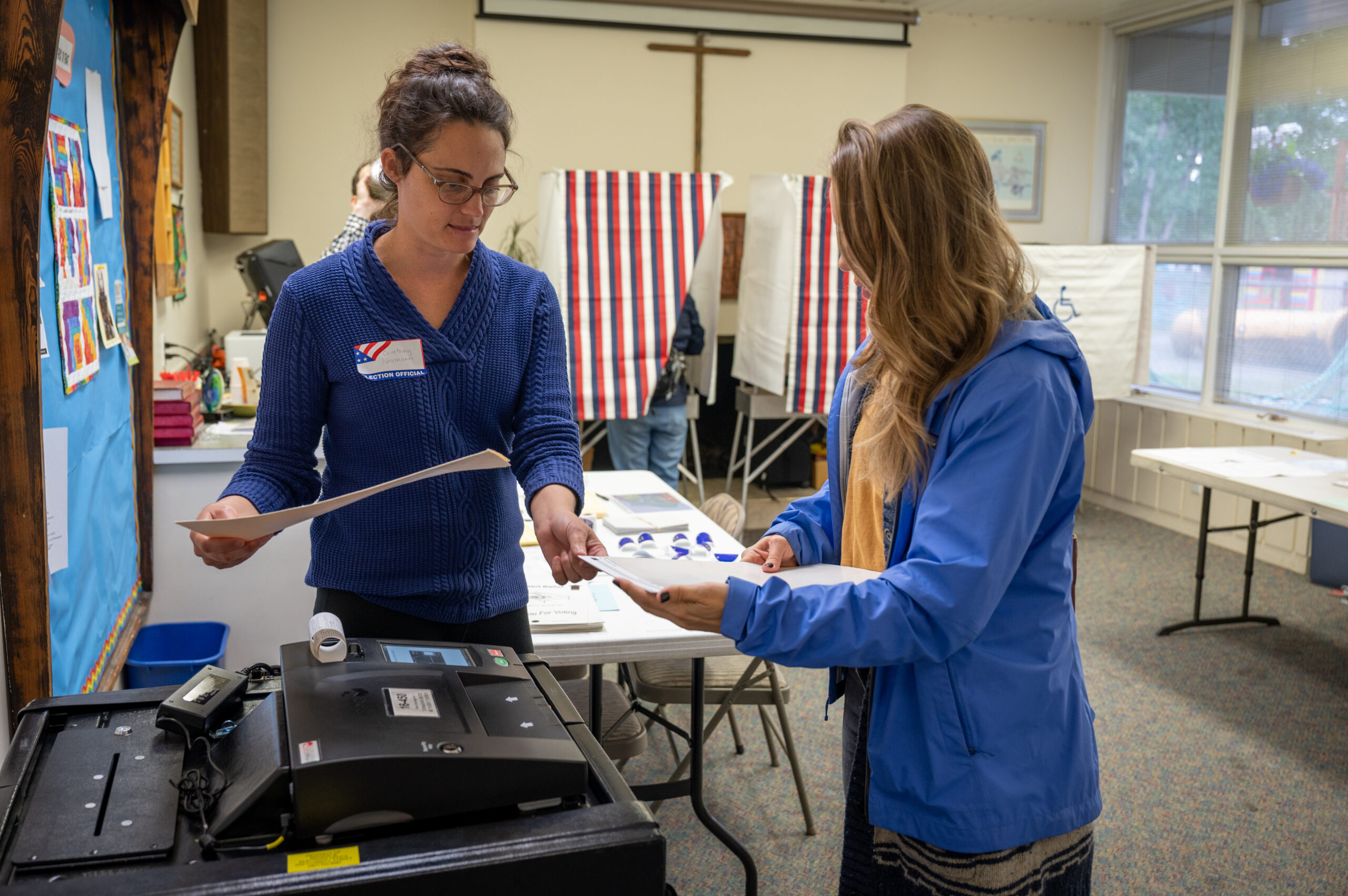 A woman in a blue shirt helping another woman with her voting ballot