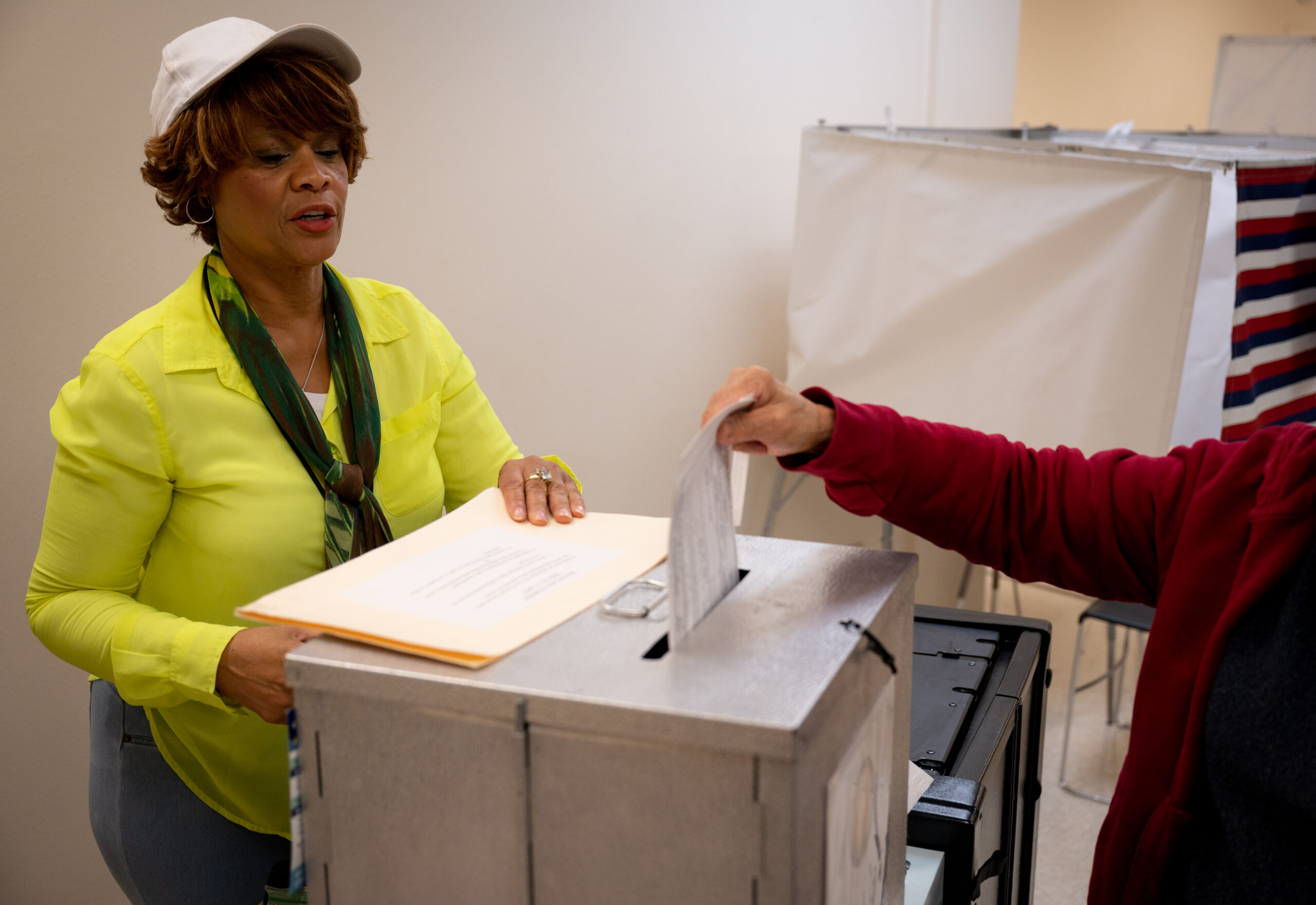 A woman in a yellow shirt stands by a silver voting box.