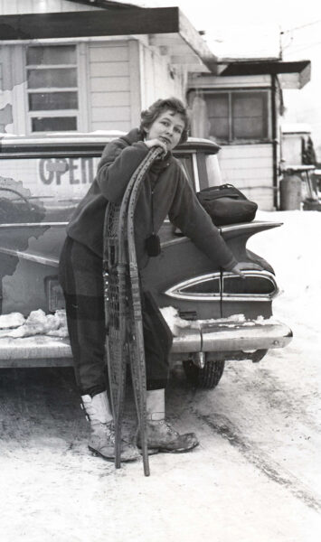 a black and white photo of a woman standing behind a car