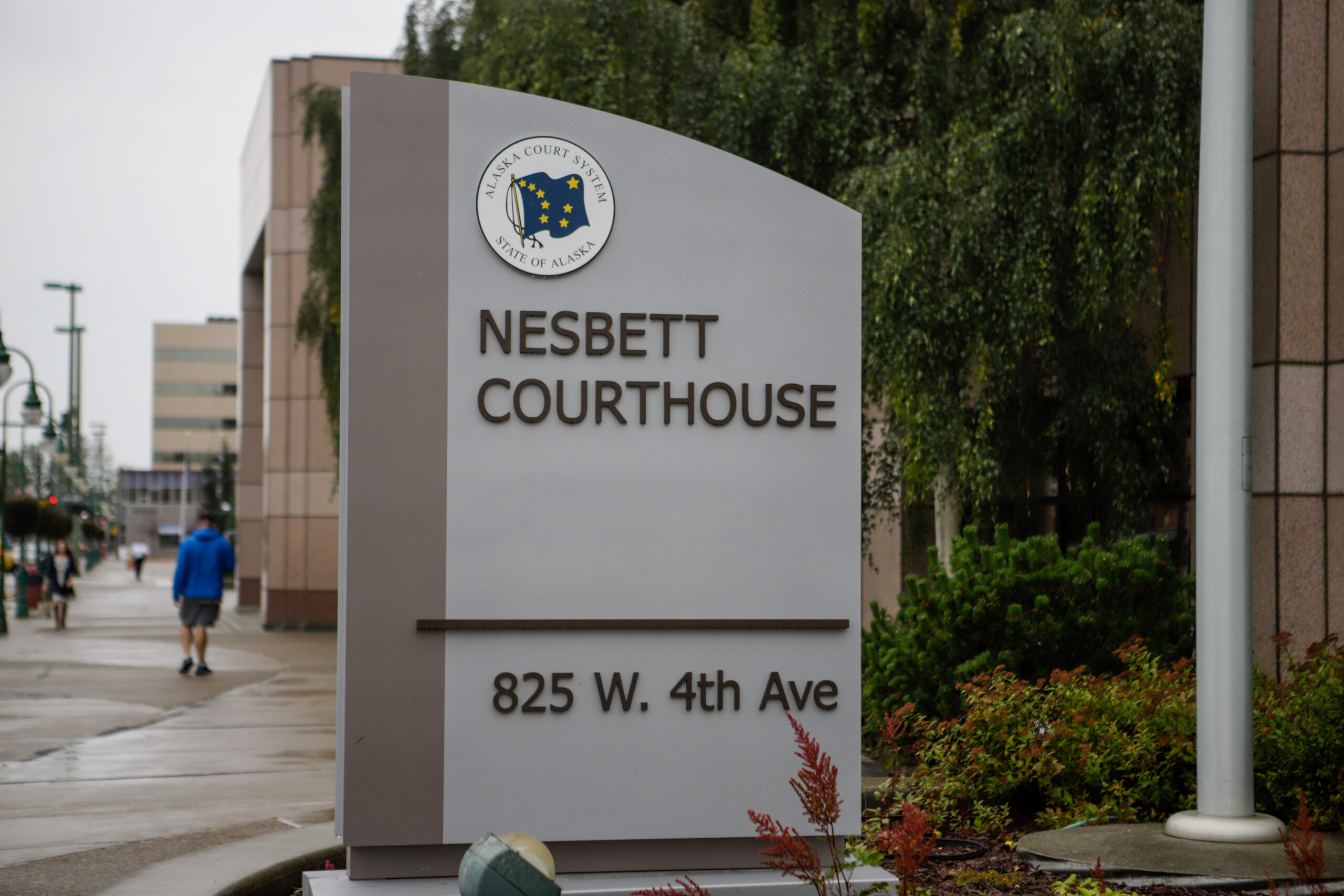 A sign reads "Nesbett Courthouse," behind the sign, pedestrians walk on the sidewalk.