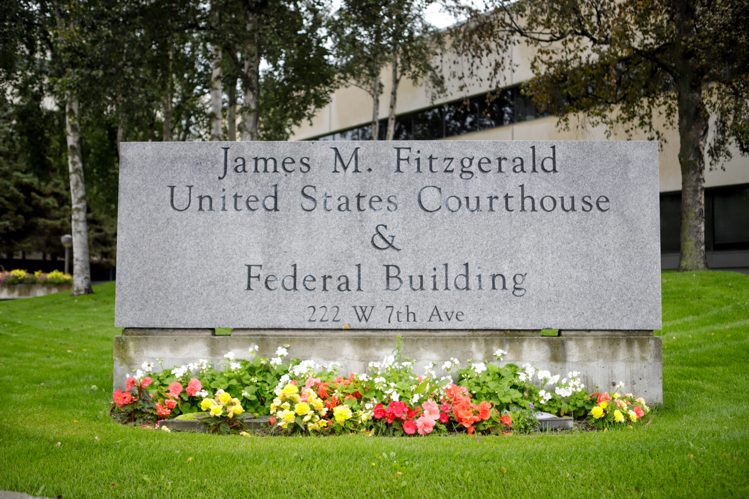 A stone sign in the middle of a lawn reads "James M. Fitzgerald United States Courthouse & Federal Building." In front of the sign are pink, yellow and orange flowers.