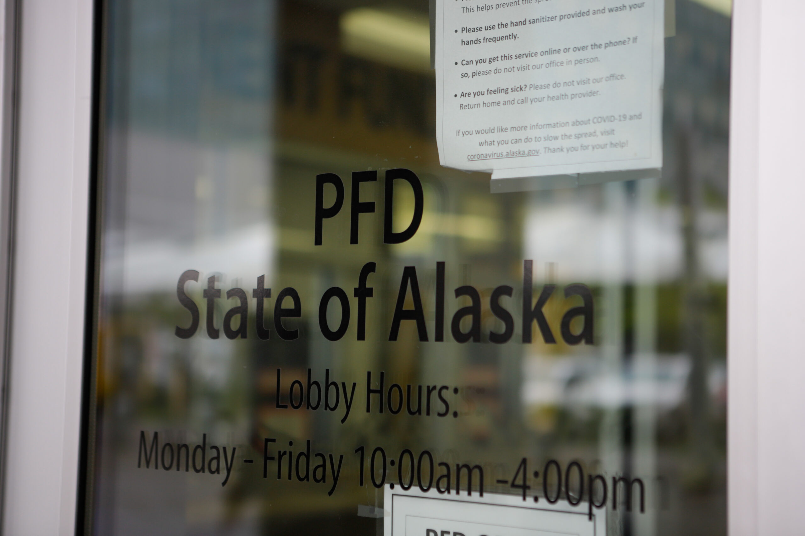 The glass door to the entrance of the PFD office. In black lettering is "PFD State of Alaska, Lobby hours Monday-Friday 10 a.m. to 4 p.m."