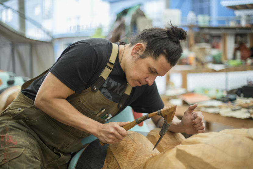 a carver carving a totem pole with an adze